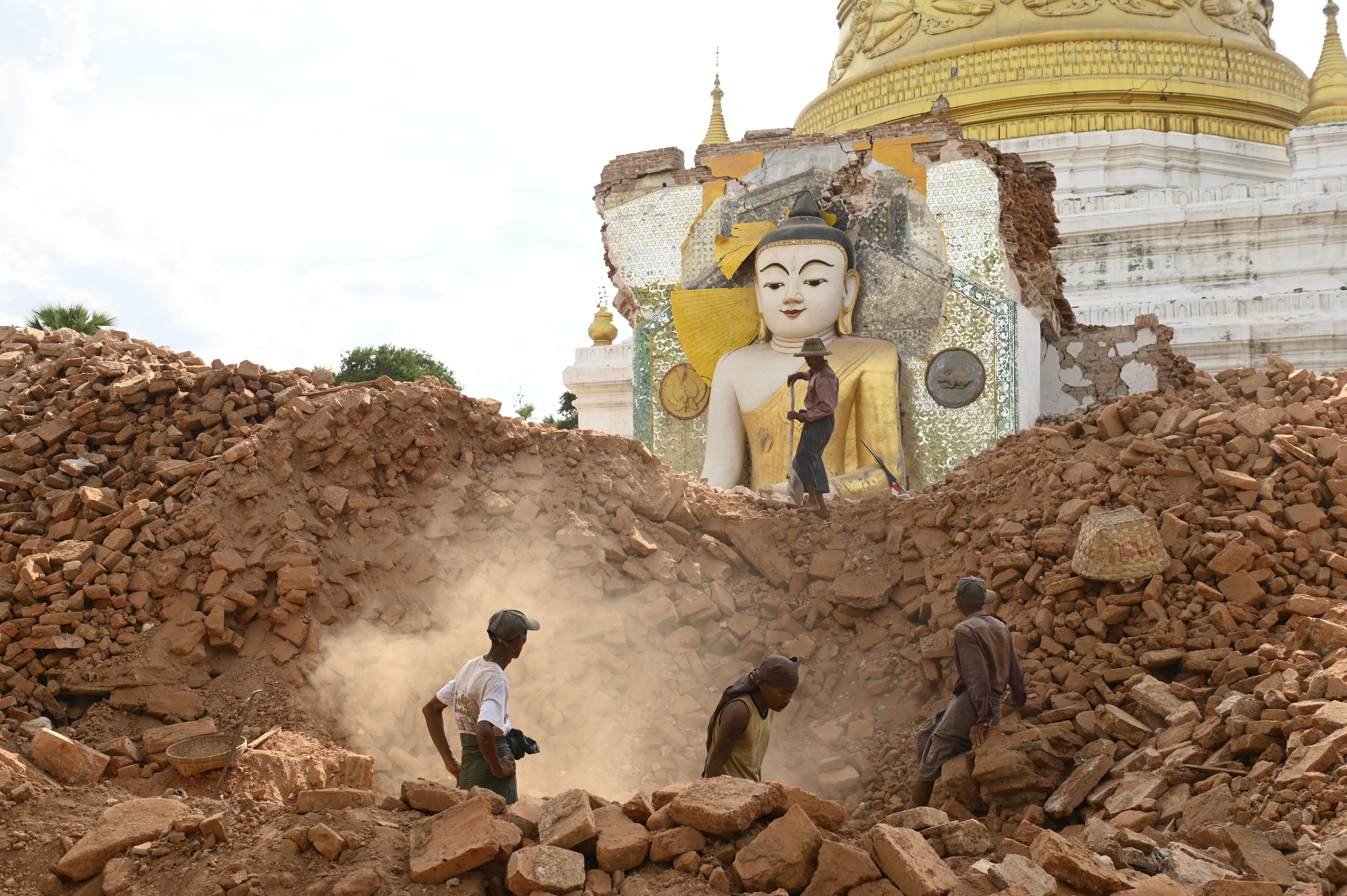People clear debris of a damaged Buddha statue at Lawkatharaphu pagoda in Inwa